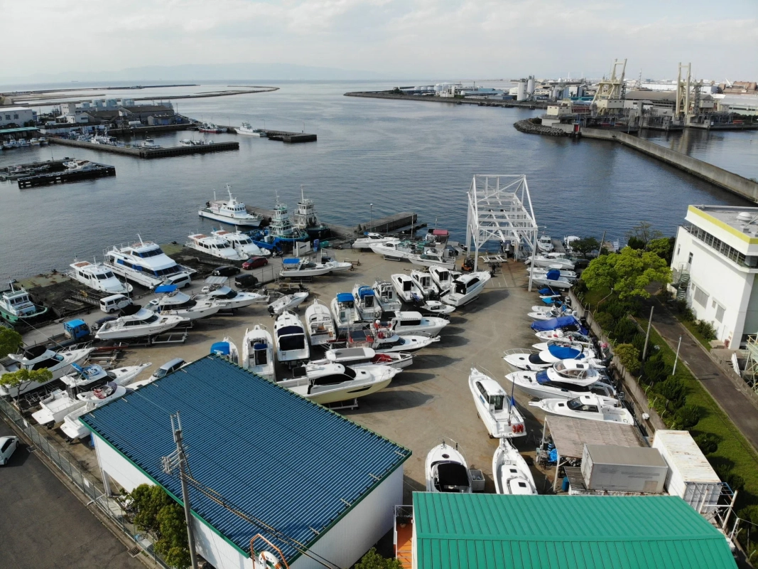湾に隣接する船の保管場所または造船所を上空から捉えた画像。多数のヨットやボートが陸上に保管されており、奥には港湾施設が見える。