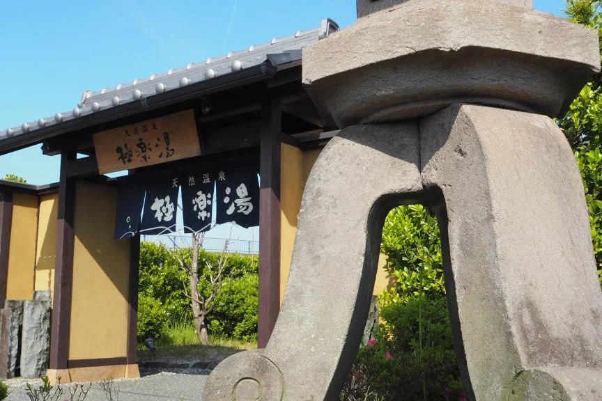 青空の下、和風の建物にある天然温泉「極楽湯」の入り口