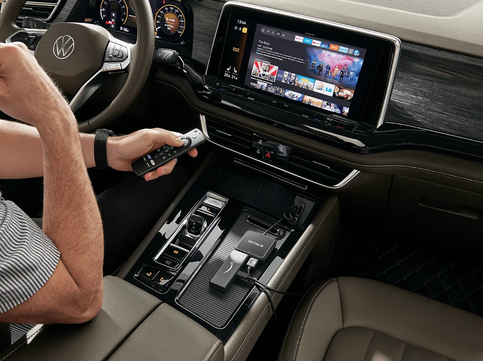 車内でAmazon Fire TV Stickのリモコンを操作し、大型インフォテインメントディスプレイでストリーミングコンテンツを視聴する様子