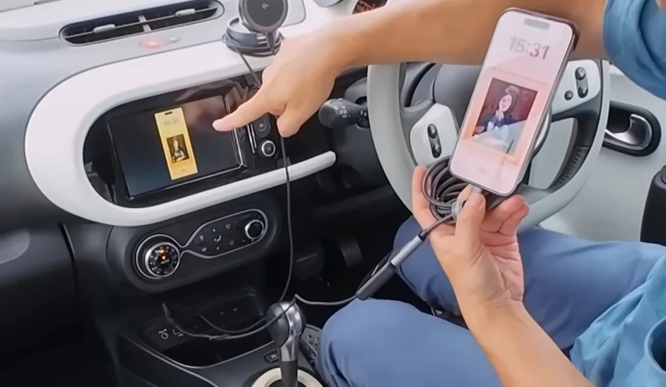 運転席に座った人物が、スマートフォンを車のインフォテインメントシステムにケーブルで接続している様子