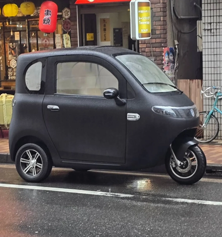雨上がりの日本の街角に駐車された黒い三輪自動車