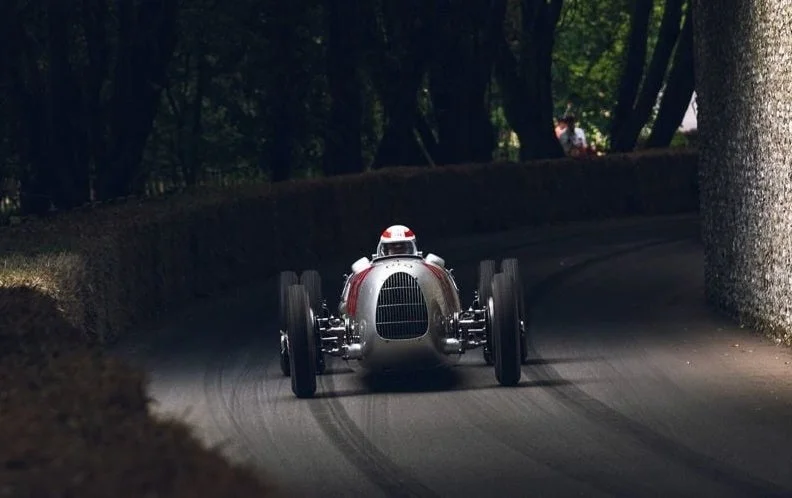 暗い森の中の曲がりくねったコースを走る銀色のヴィンテージレースカー