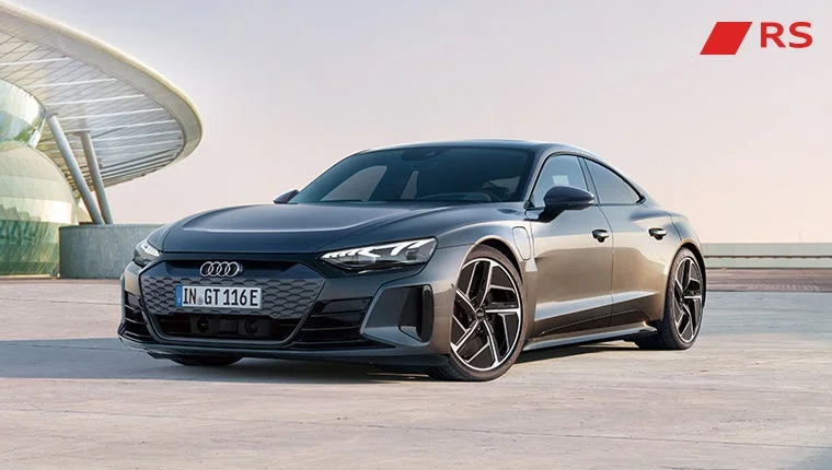 アウディのダークグレーのe-tron GTが、モダンな建築物を背景にした屋外に駐車されている