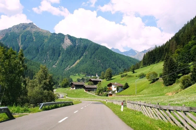 緑豊かな山々に囲まれた谷間を曲がりくねった道路が走り、牧歌的な家々が点在する美しい夏の風景