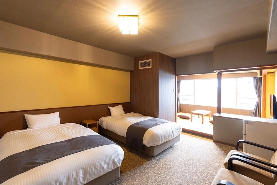 ツインベッドが2台置かれたホテルの客室。窓際には座卓と座布団がある和風のくつろぎスペース
