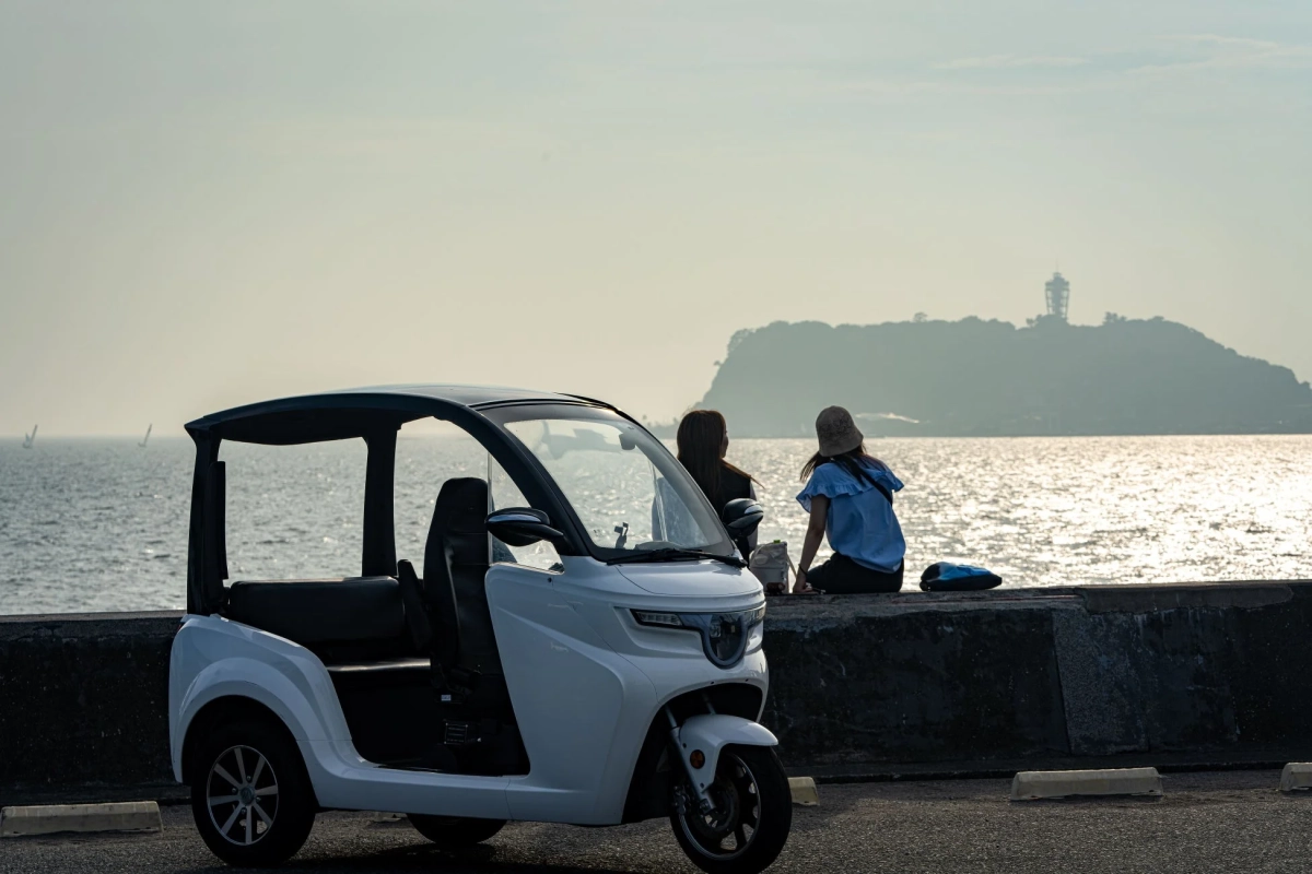 海岸で夕暮れの海を眺める女性たちと電動トゥクトゥク