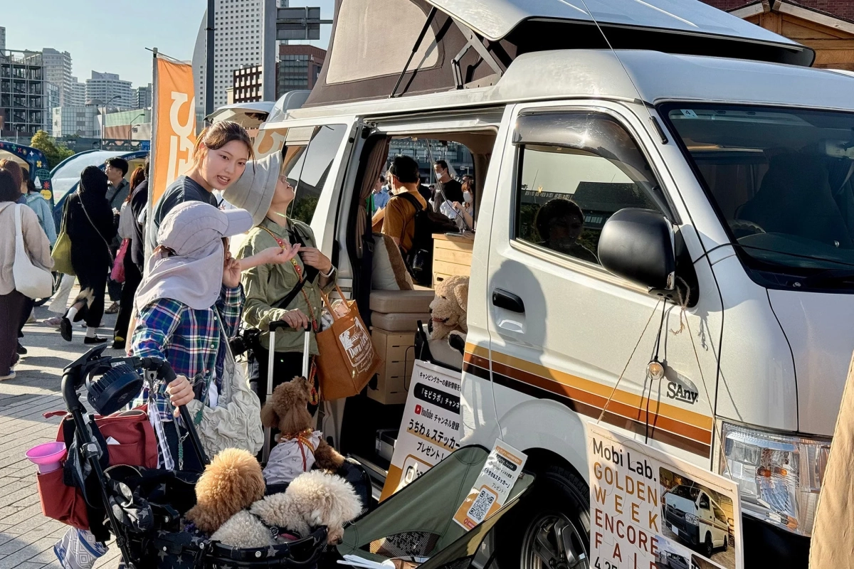 ゴールデンウィークのイベント会場で、ポップアップルーフのキャンピングカーが展示されています。多くの来場者がおり、犬を連れた家族も見られ、賑やかな雰囲気です。
