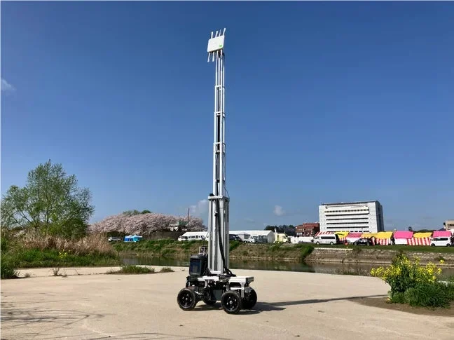 青空の下、河川敷に設置された車輪付きの移動式基地局ロボットの画像です。