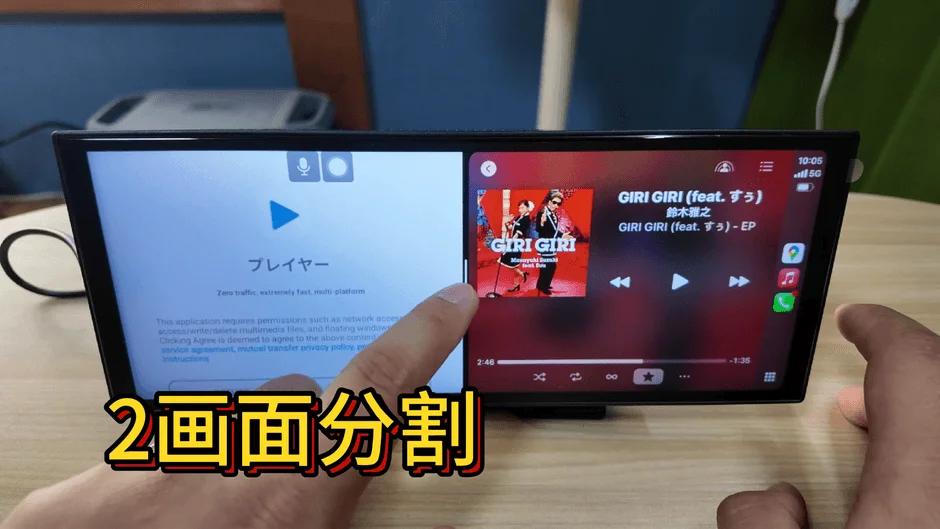 「２画面分割」と表示されたポータブルディスプレイで、左側にはプレイヤーアプリの利用規約、右側には鈴木雅之の楽曲「GIRI GIRI」が再生されている様子が映し出されています。指が画面に触れており、操作中のようです。