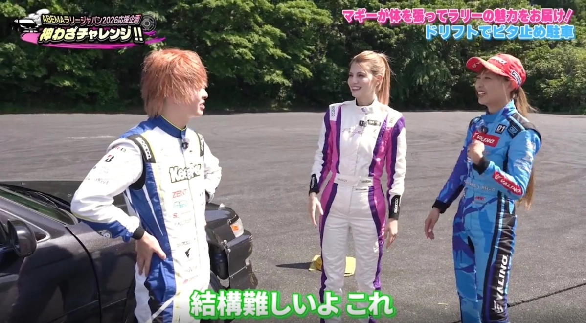 レーシングスーツを着た3人が屋外のアスファルト上で車と共に立っています