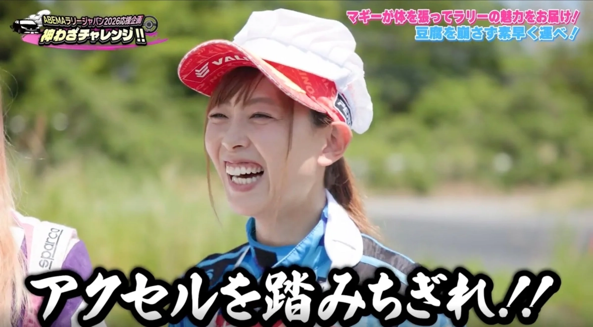 マギーさんがレーシングスーツ姿で笑顔を見せています