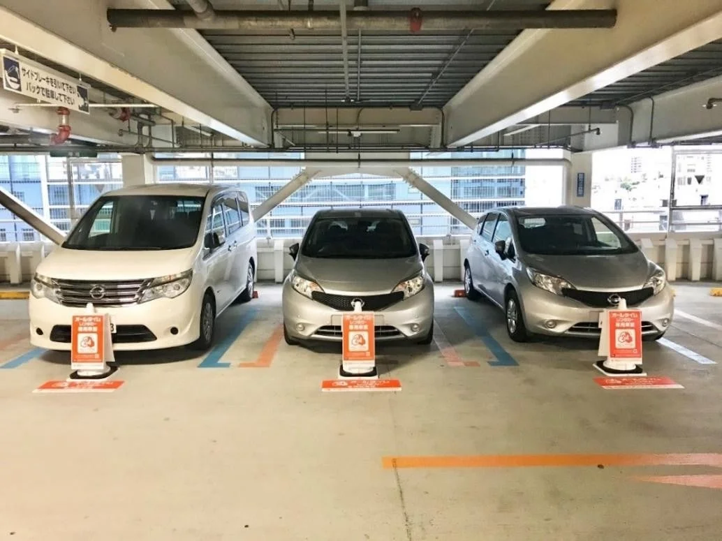 屋内駐車場に停められた3台の日産車（セレナ1台、ノート2台）のカーシェア車両が写っています。各車両の前には利用を示すコーンが置かれ、駐車に関する注意書きも見られます。