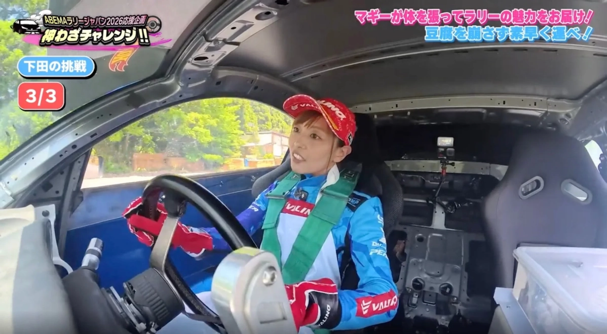 女性ドライバーがラリーカーの運転席に座り、真剣な表情でハンドルを握っています