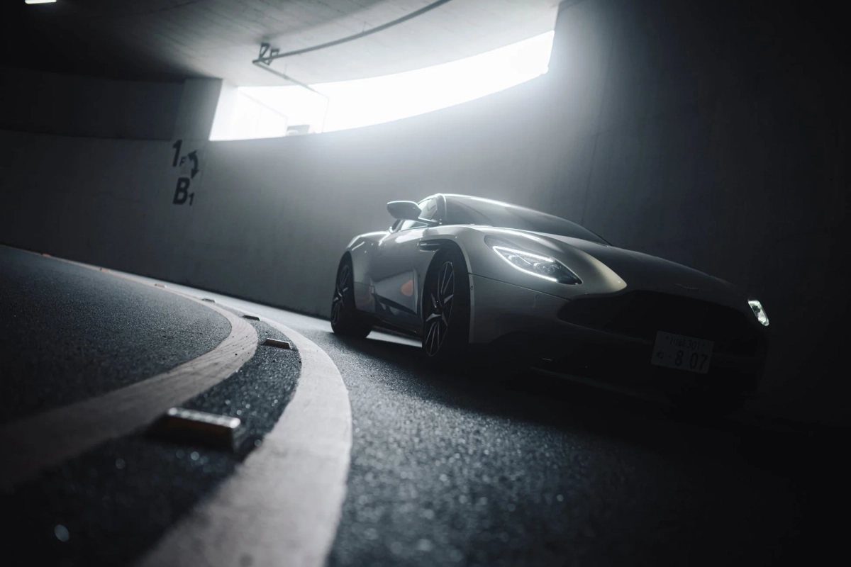 薄暗いトンネルのカーブを走行するシルバーの高級スポーツカー。上部からの強い光が車体を照らし、スタイリッシュで未来的な雰囲気を演出しています。