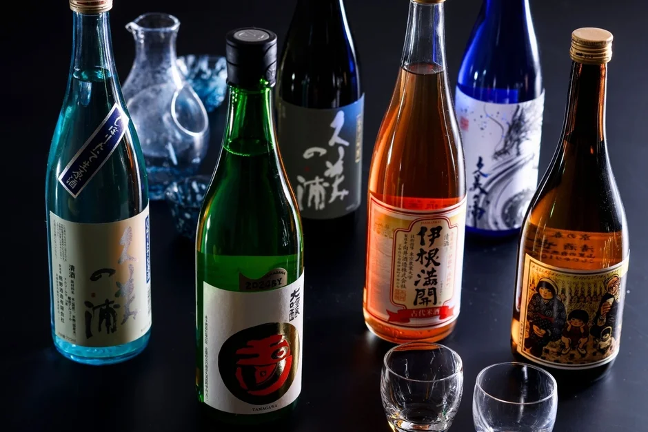様々な色やラベルデザインの日本酒ボトルが複数並べられています。