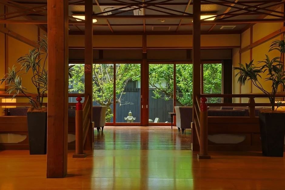 木造の日本家屋の廊下から、青々とした日本庭園を望む穏やかな風景。