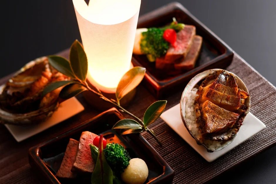 高級感のある和風の膳に、アワビの炊き込みご飯や牛肉料理などが美しく盛り付けられています。