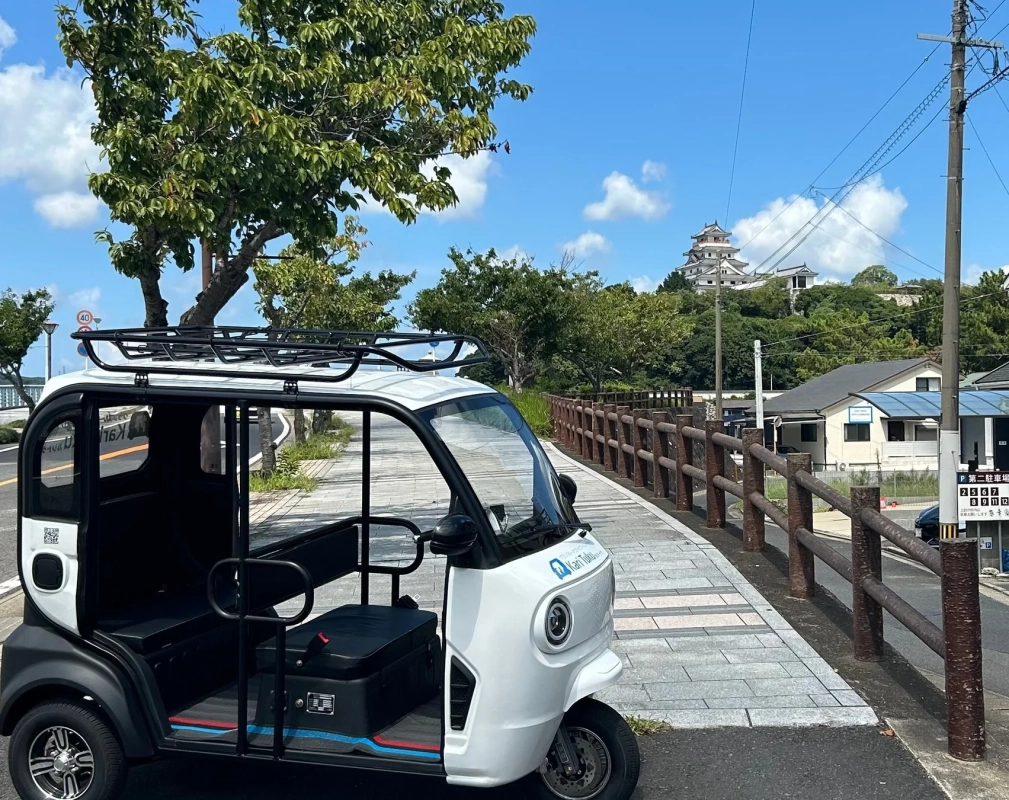 青空の下、白い電動ミニカーと日本の城郭