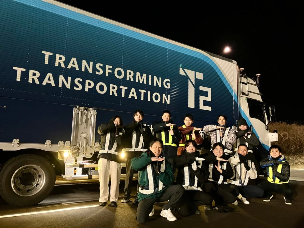 夜間、大型トラックの前で反射ベストを着用した人々がポーズをとって写る集合写真